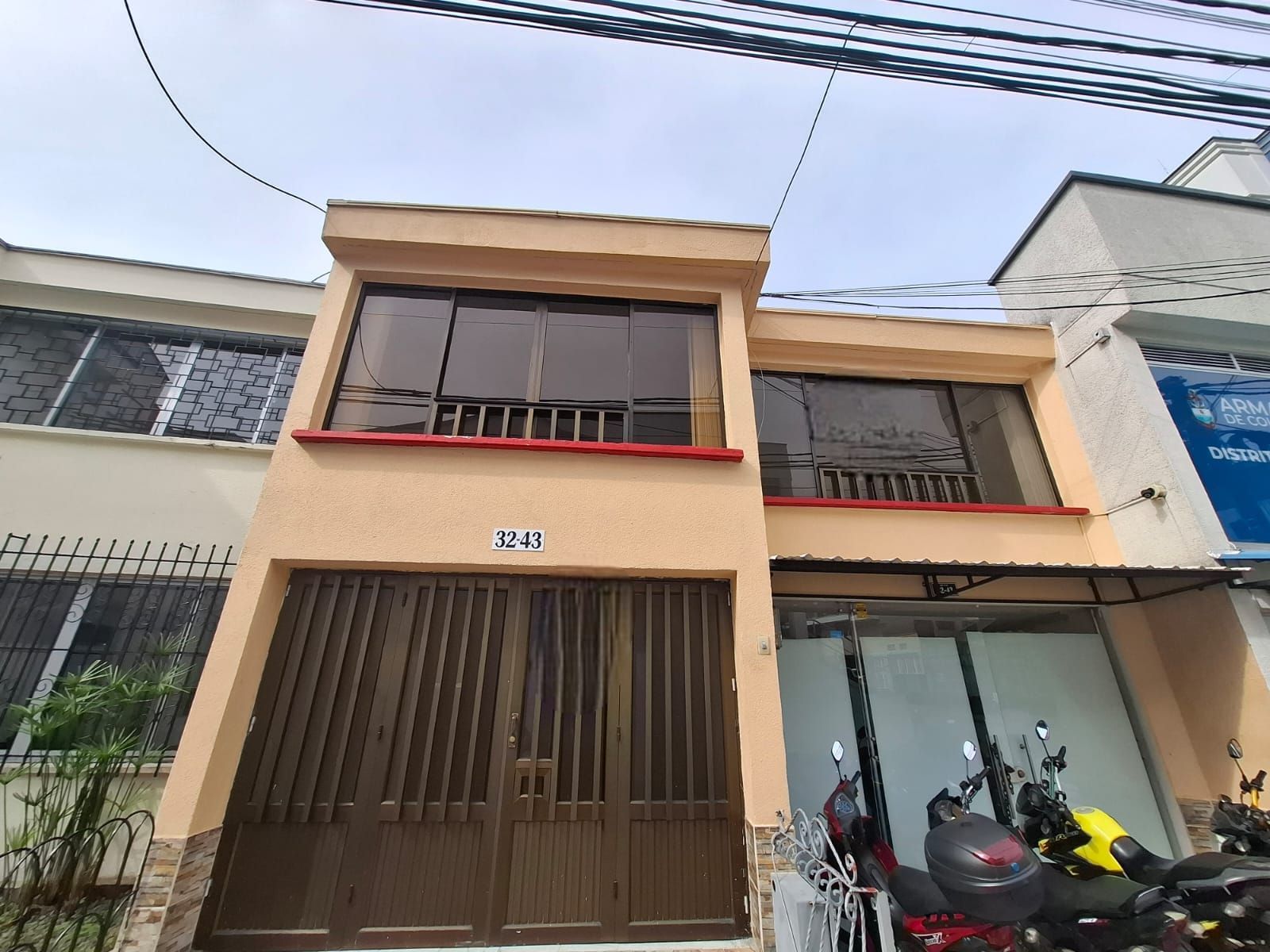 Casa beige de dos plantas con puerta y balcón marrones, motos aparcadas delante en una calle estrecha.