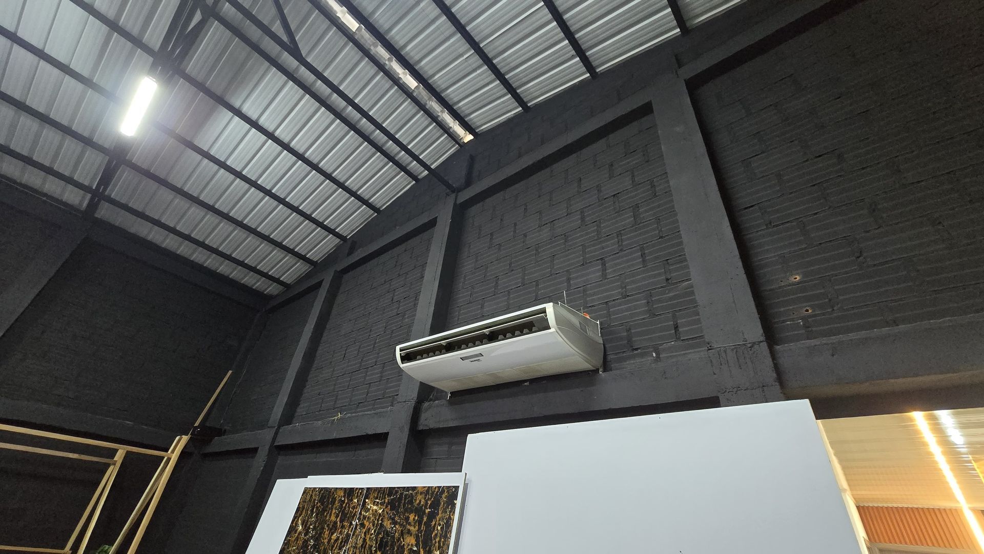 Interior industrial con paredes oscuras, techo alto de metal y un aire acondicionado montado en la pared sobre una división.