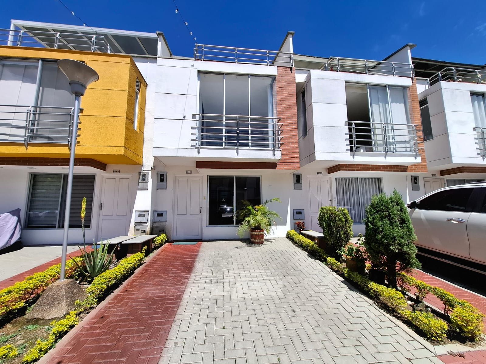 Hilera de casas adosadas modernas con fachadas blancas, entradas de ladrillo rojo y un coche aparcado delante.