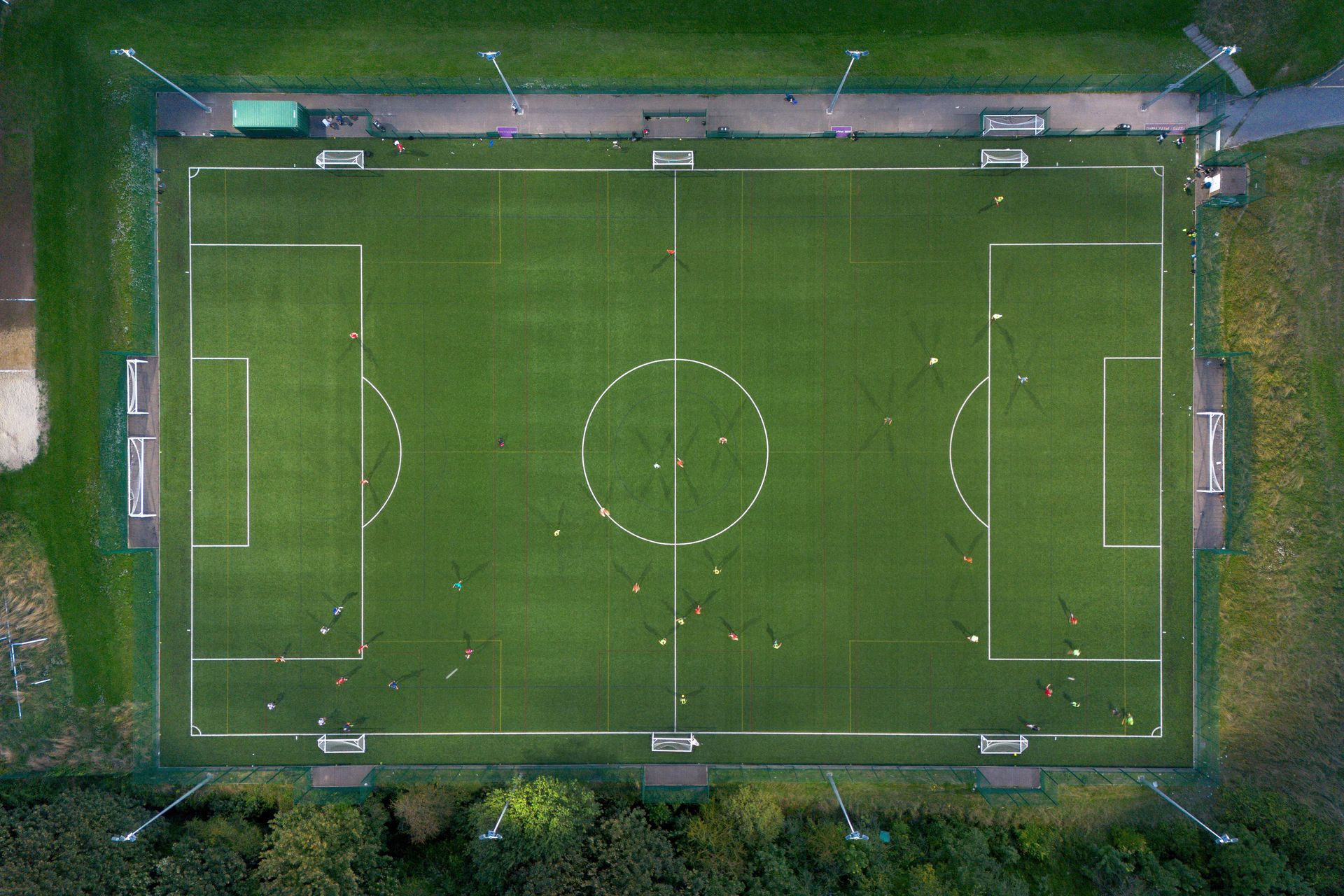 Aerial view of an empty green soccer field with white boundary lines and goal areas.