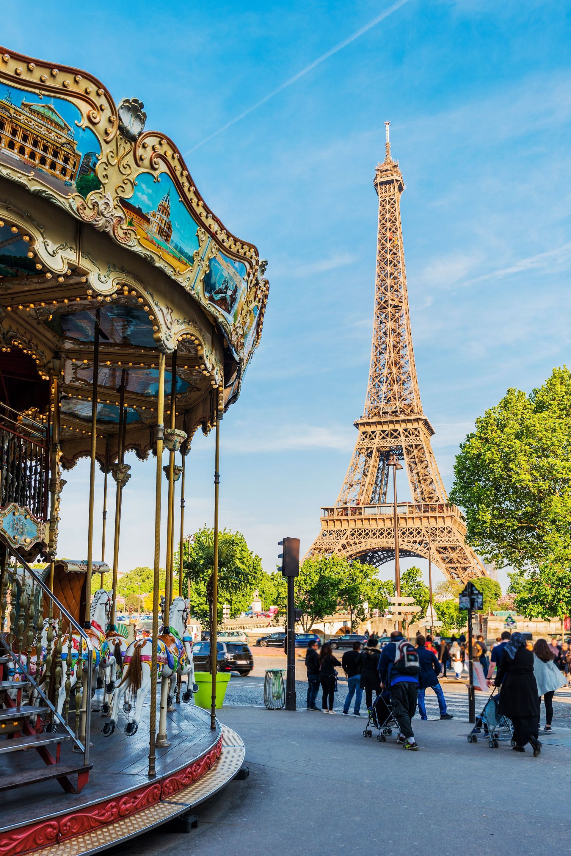 Eiffel Tower behind a carousel in a sunny Paris plaza with pedestrians and trees