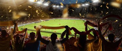 Crowd cheering in a brightly lit soccer stadium at night, with fans raising arms and flags