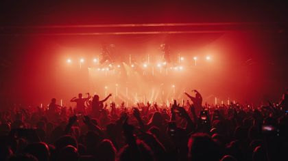 Crowd at a concert with raised hands under bright red stage lights and haze