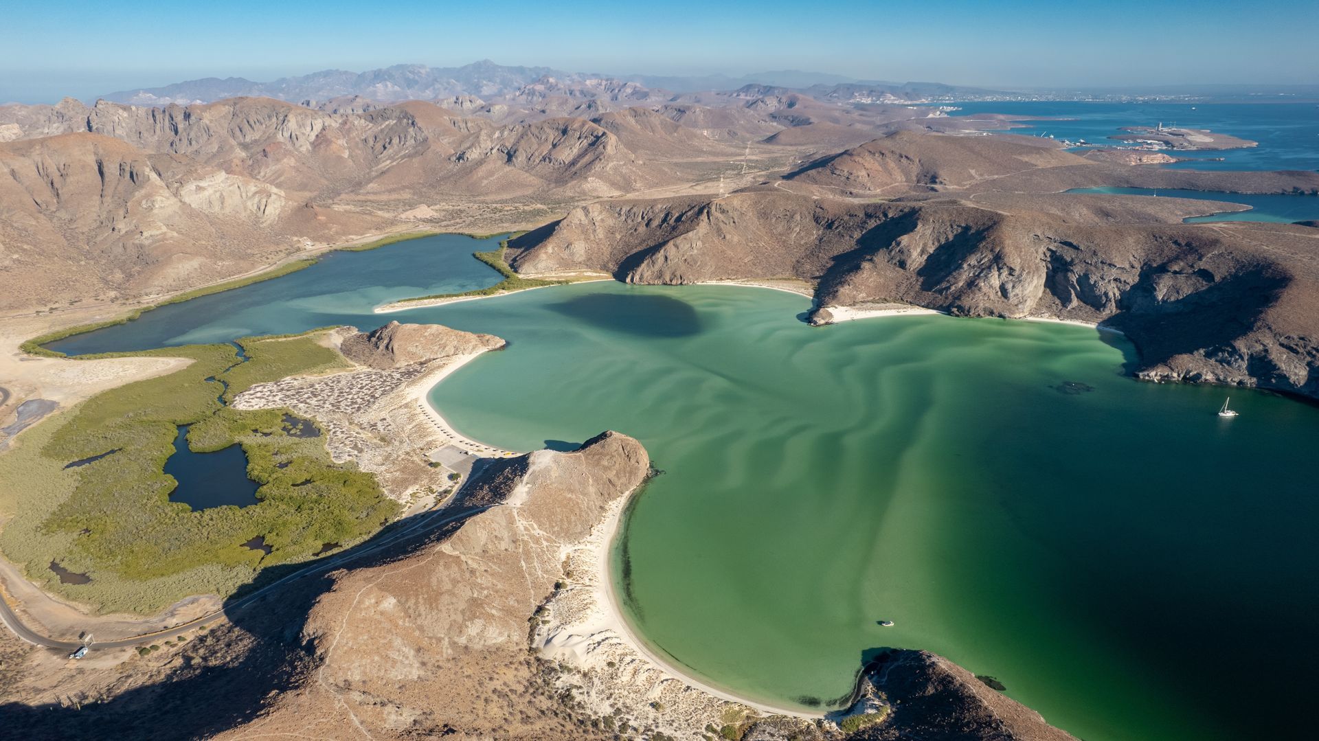 Aerial view of a green coastal bay with rocky mountains and a small sandy peninsula