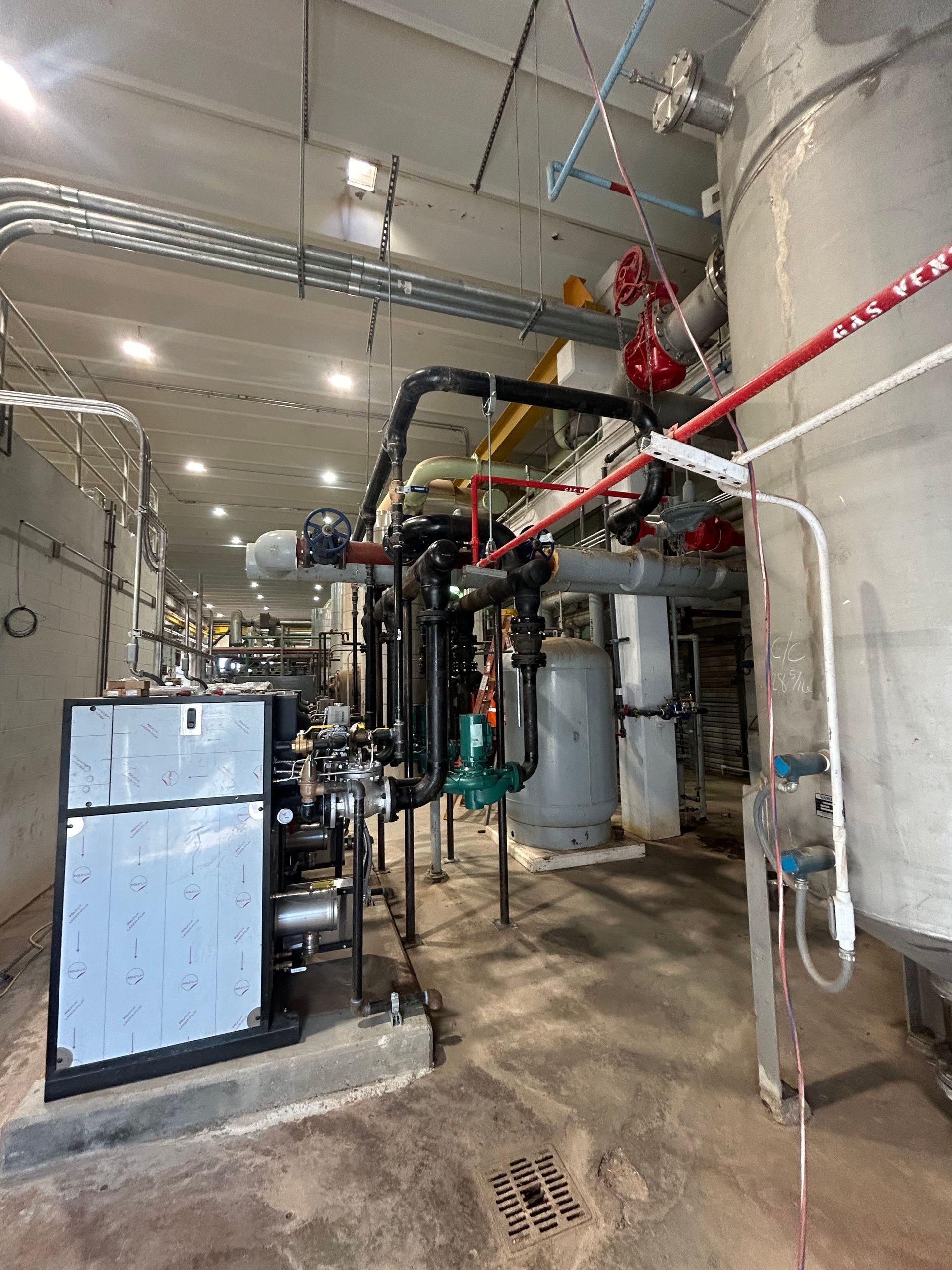 Industrial machinery and piping in a concrete room with several tanks and pipes.