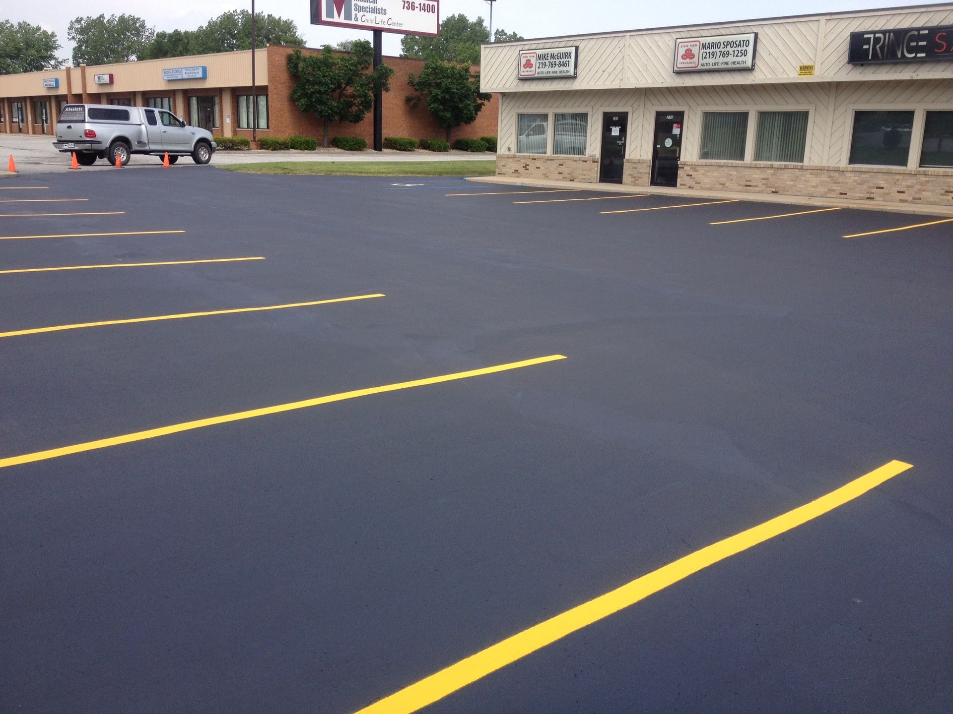Newly paved parking lot with yellow parking space lines. A pickup truck is parked in the distance.