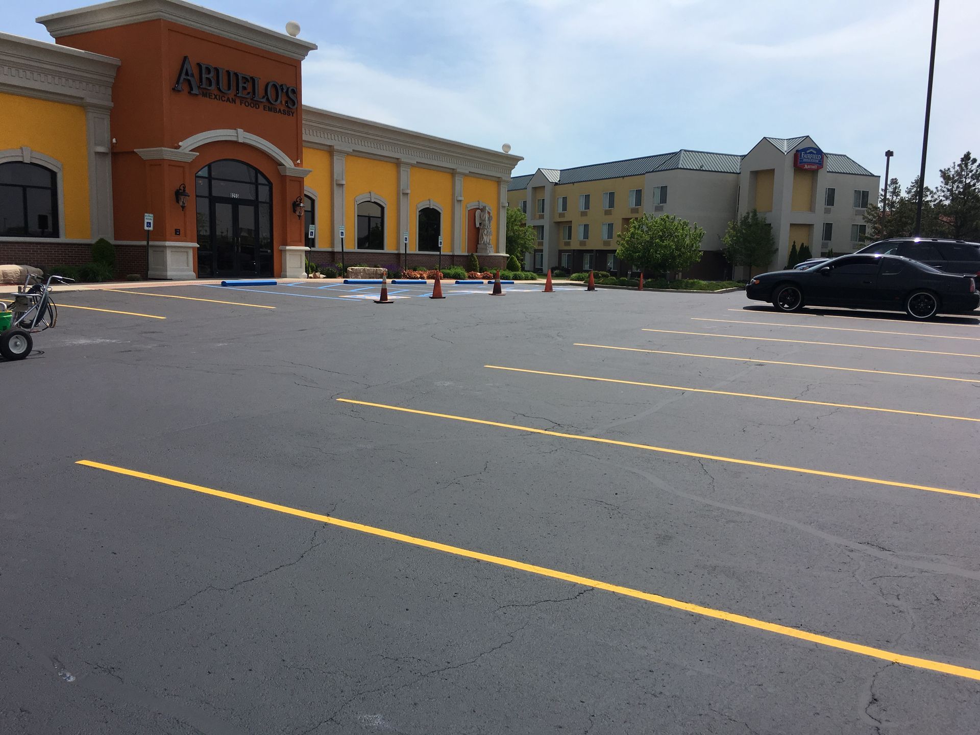 Asphalt parking lot in front of a building with orange awning, with parking lines and orange cones.