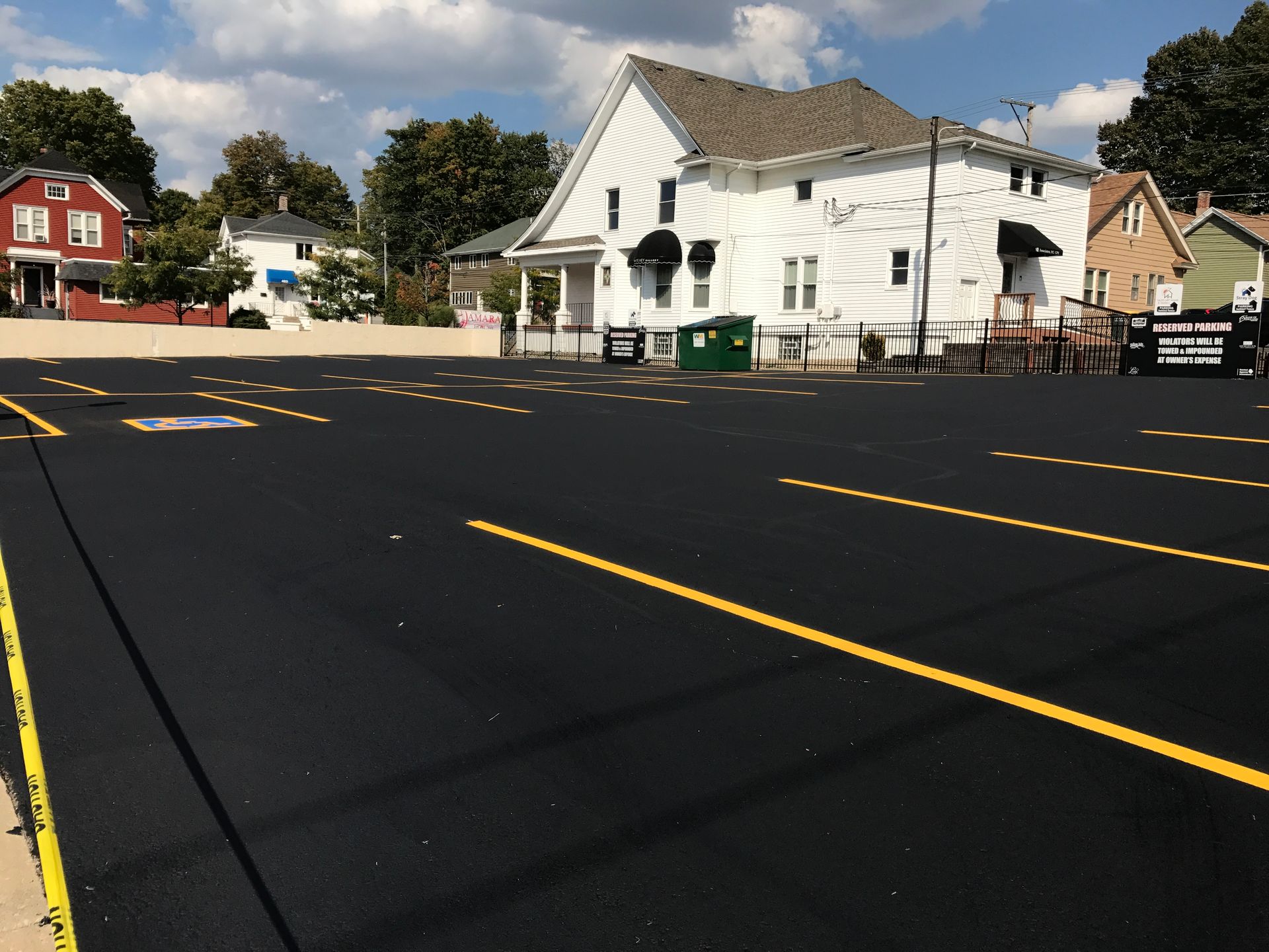 Black asphalt parking lot with yellow lines, two-story white building in background.