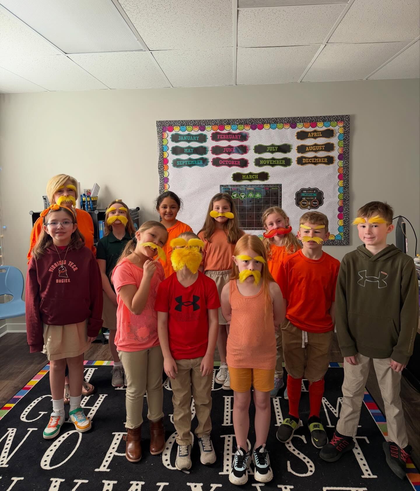 Students wearing colorful masks stand in a classroom, posing in two rows.