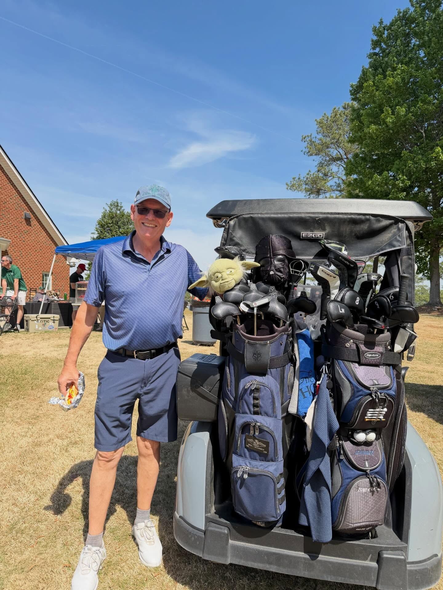 Man standing beside a golf cart loaded with golf bags on a sunny day
