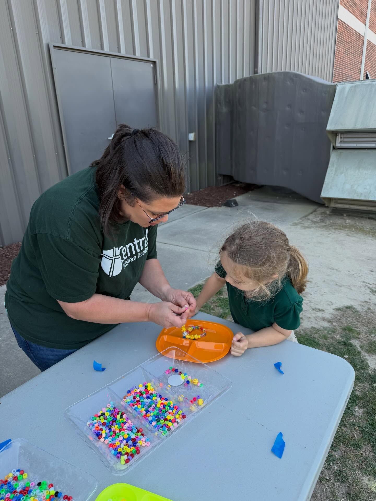 Adult and child making a craft on a table with colorful beads outdoors