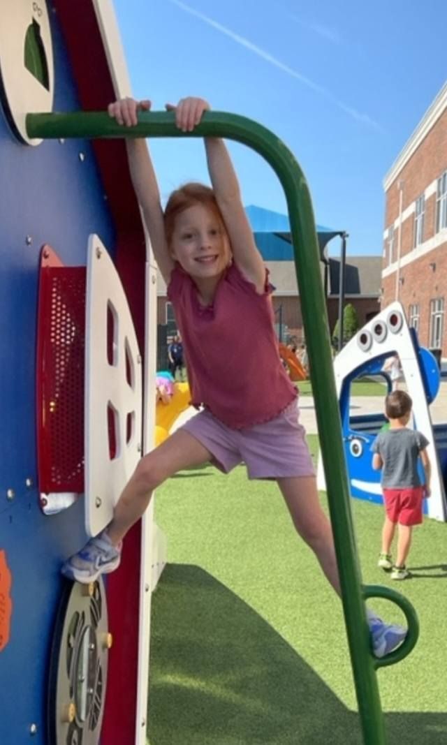 Child climbing green playground bars beside a colorful play structure on a sunny day