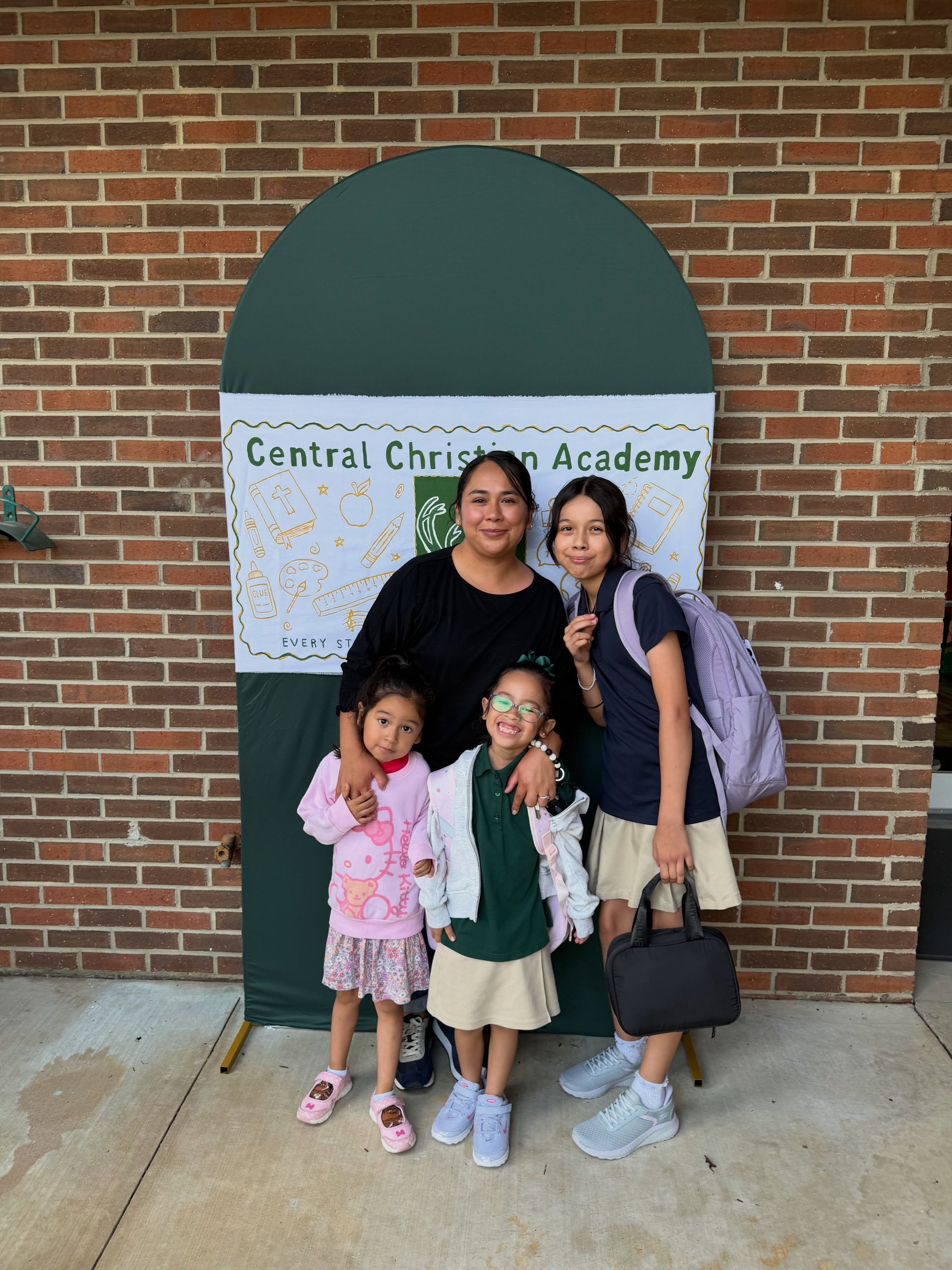 Four people pose outside Central Christian Academy in front of a brick wall and green awning.
