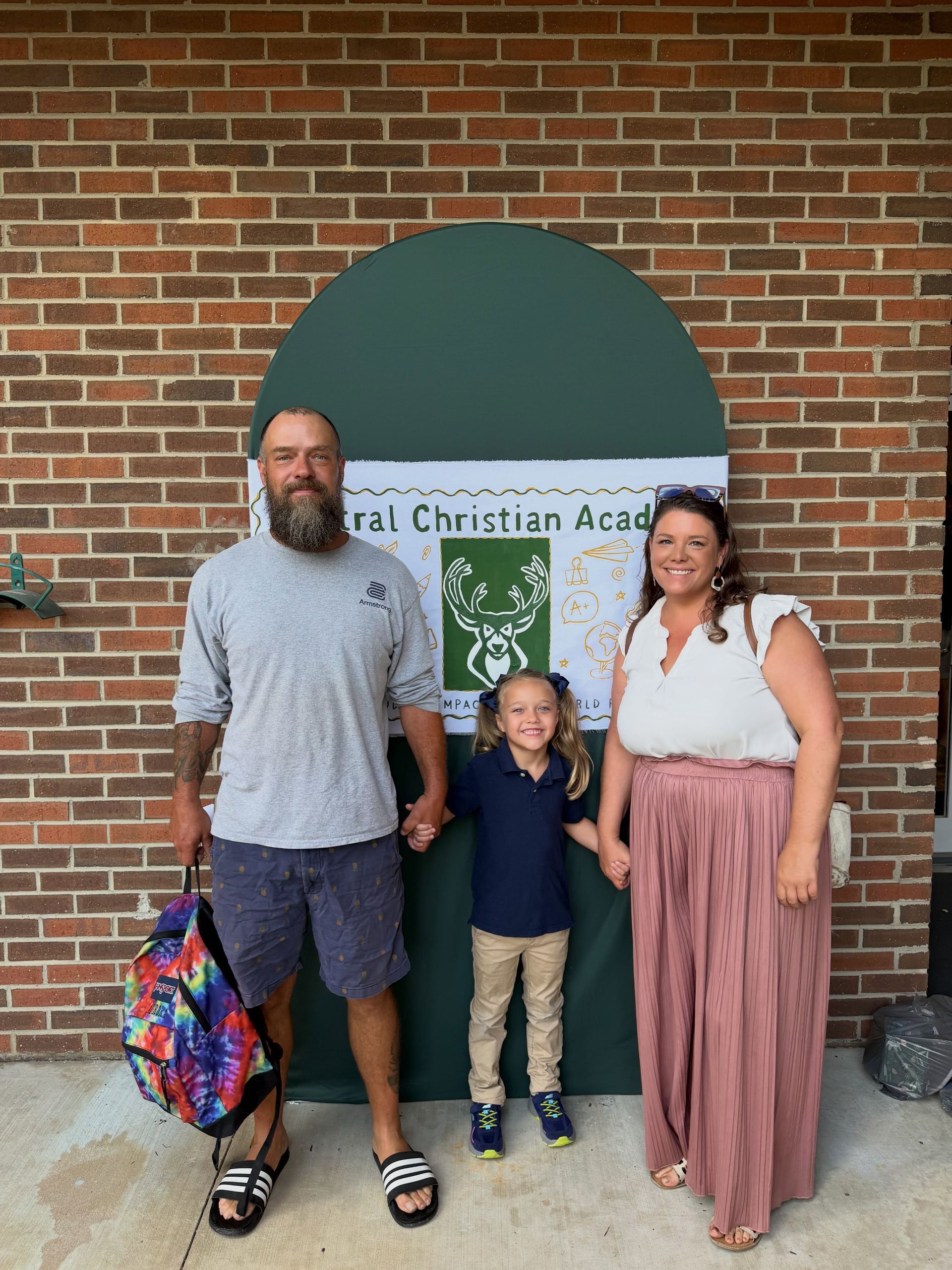 Three people standing outside Central Christian Academy in front of a brick wall and green awning