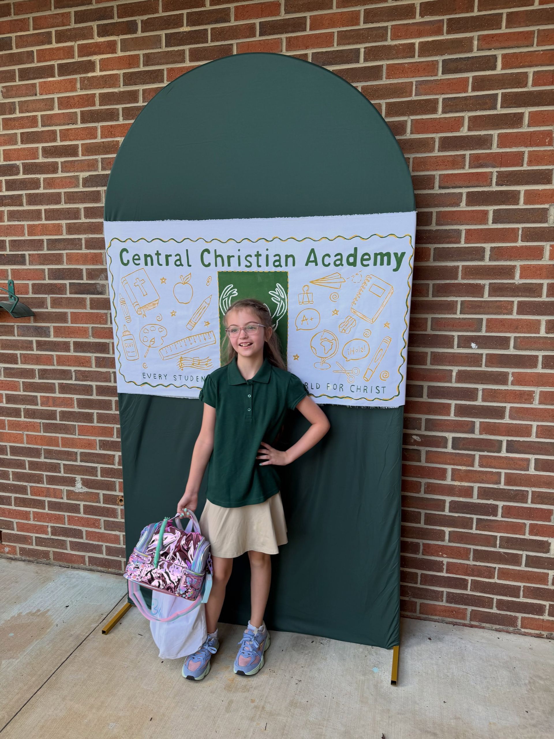 Child standing in front of Central Christian Academy banner against a brick wall