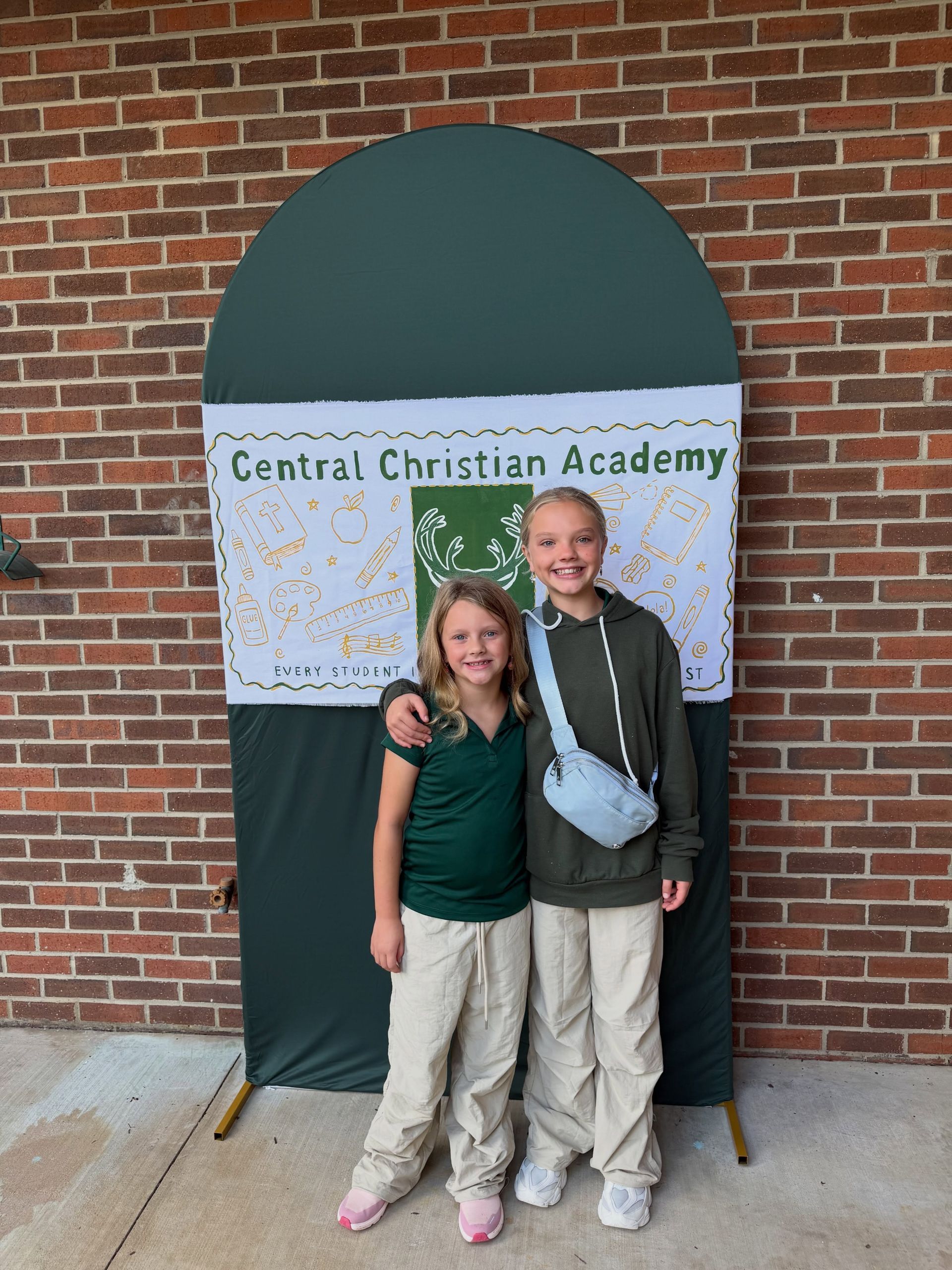 Two students standing by a Central Christian Academy sign in front of a brick wall