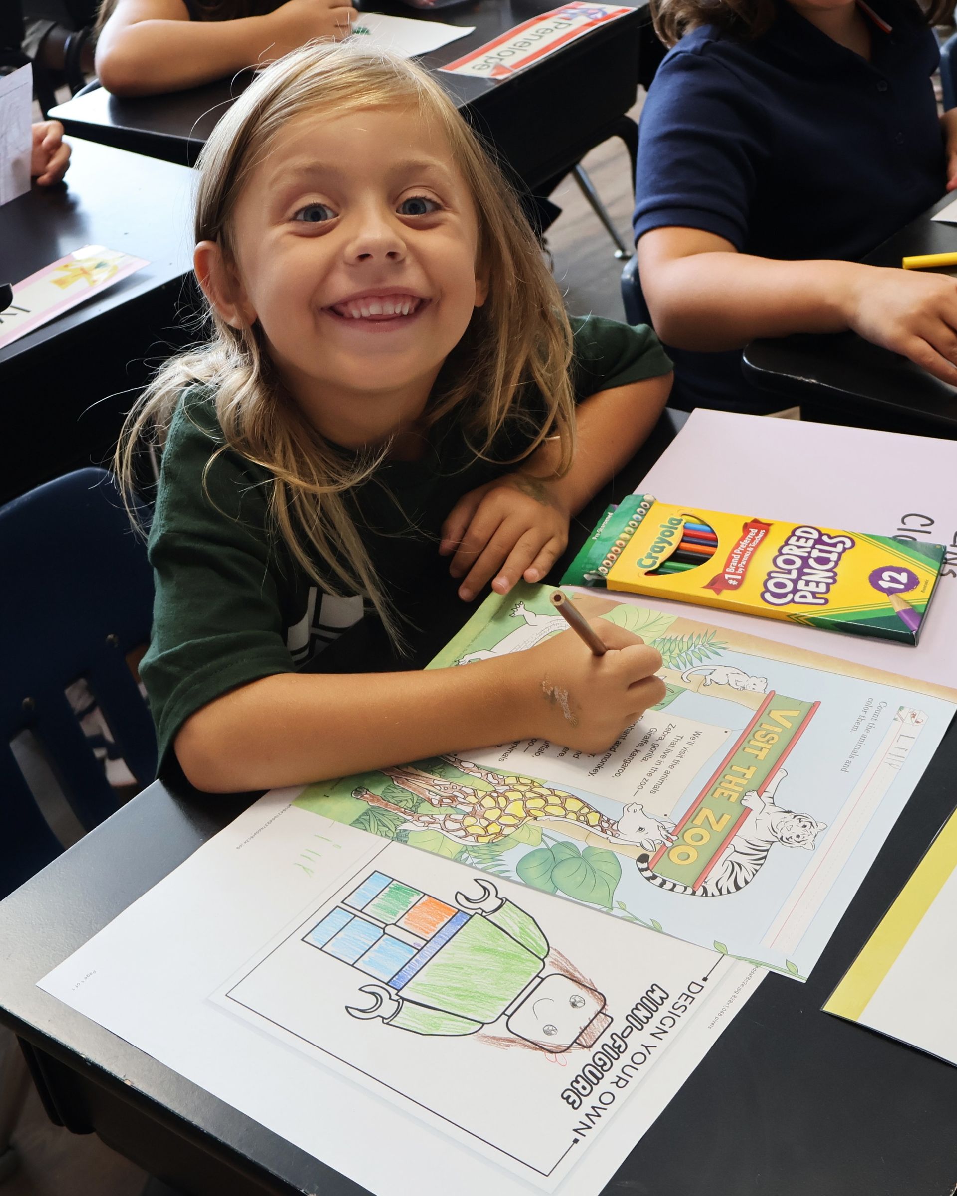 Child in a classroom holds a painting of a desert scene with figures and buildings.
