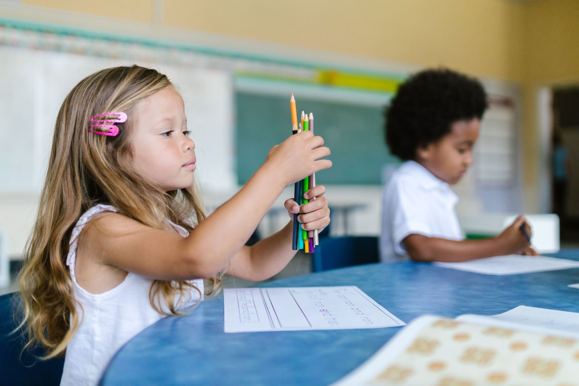 Child smiling at a table, coloring with markers and crayons in a classroom.