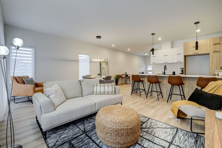 Salon moderne avec canapé, îlot de cuisine et tons neutres.