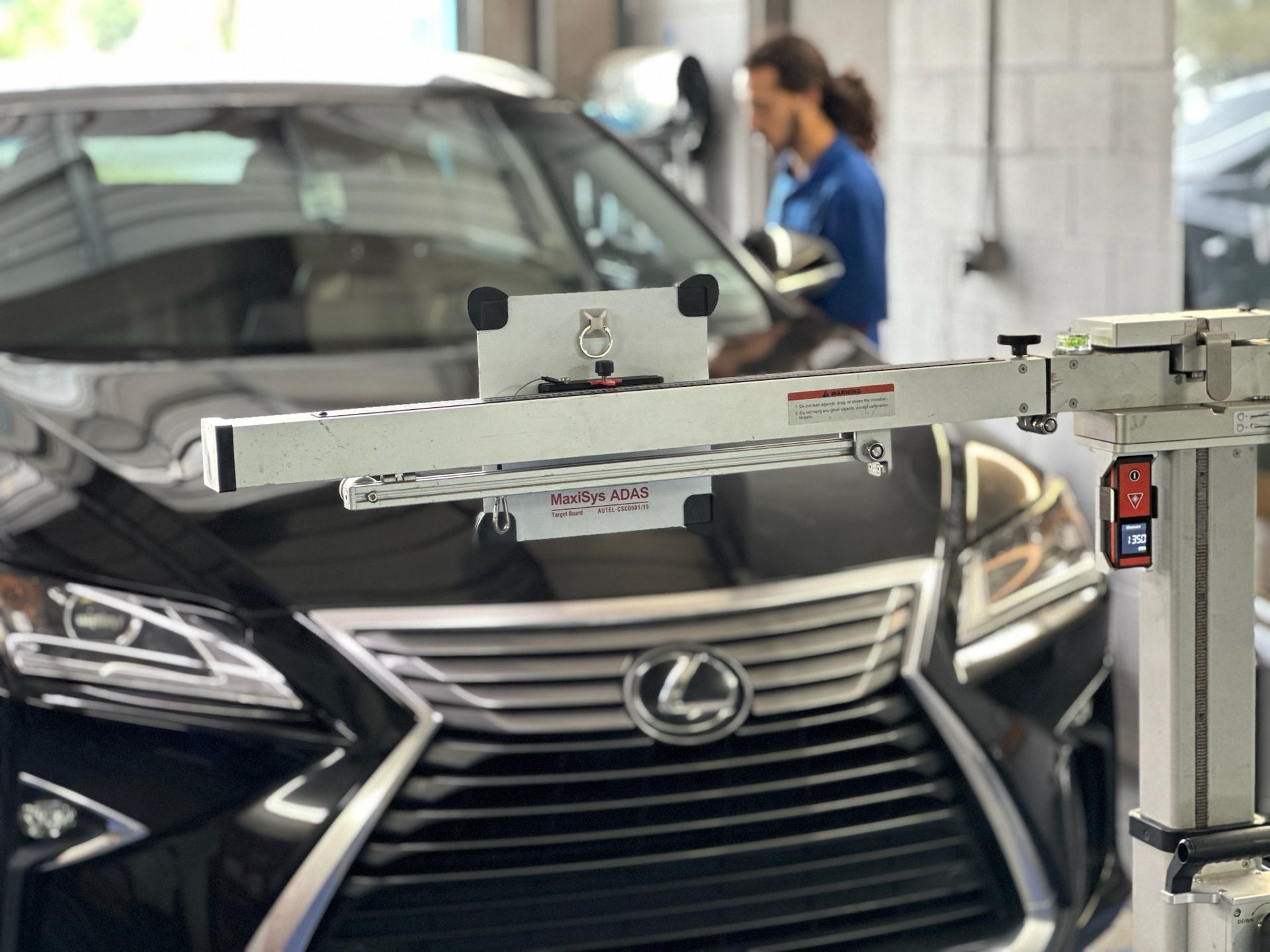 A black lexus is having a forward facing camera calibrated in a garage.