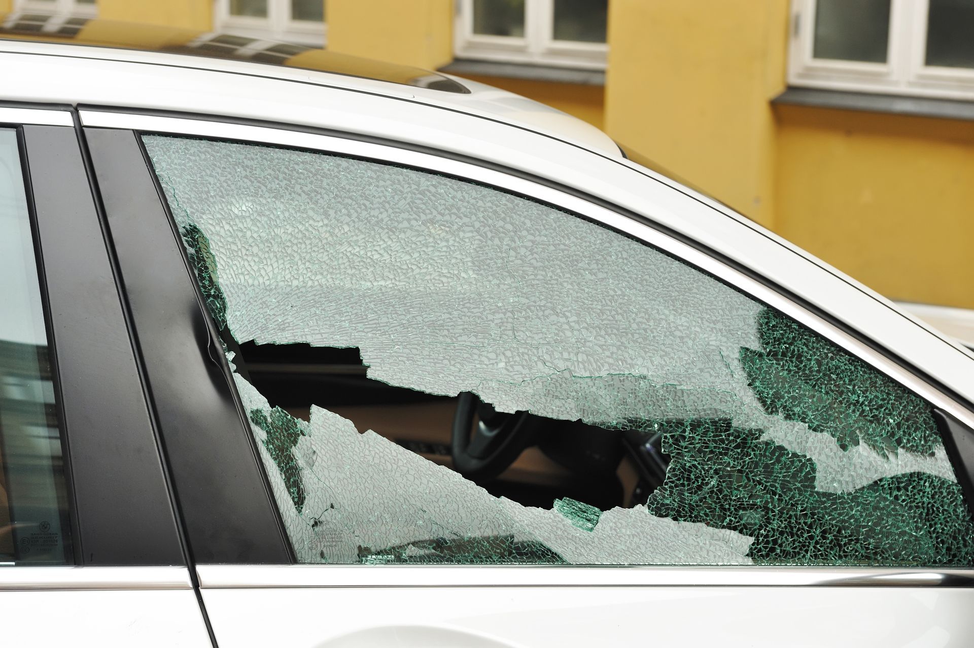 A car with a broken door glass is parked in front of a building