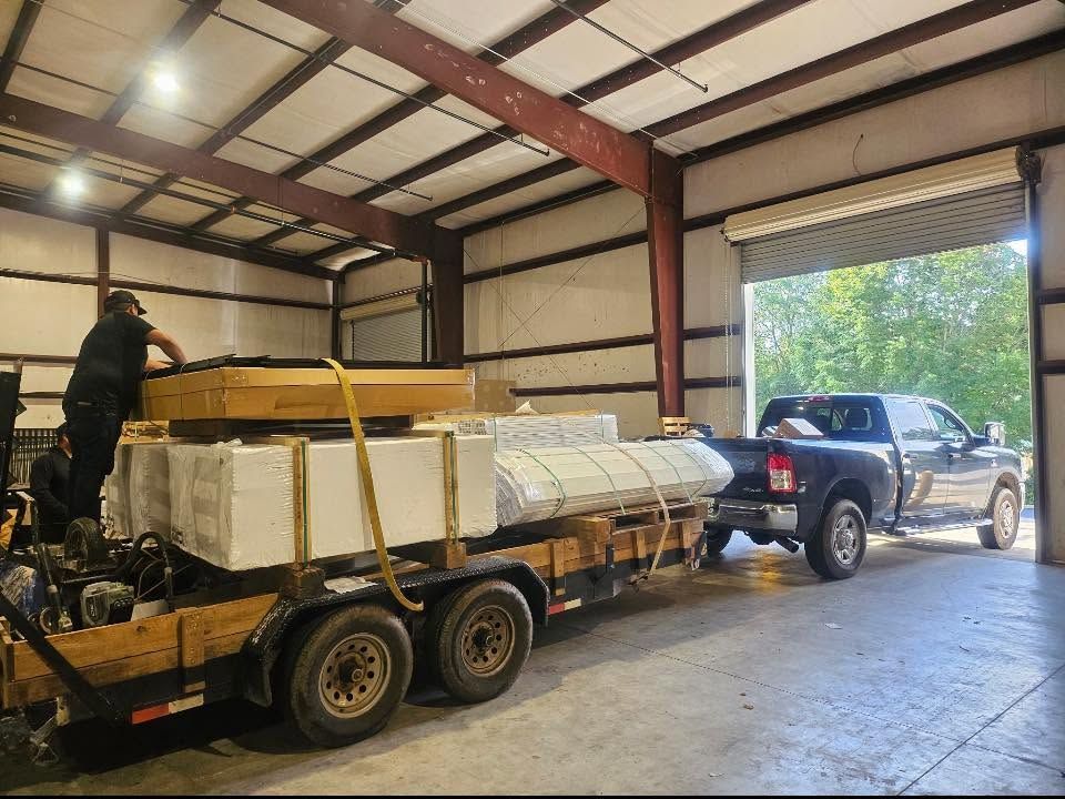 Pickup truck towing a loaded flatbed trailer inside a warehouse with a man standing on it
