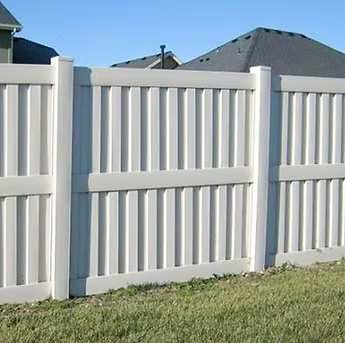 White vinyl privacy fence with gray posts along a grassy yard under a clear sky