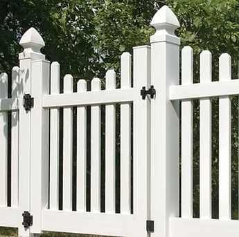 White wooden picket fence with pointed posts and black hinges against green trees