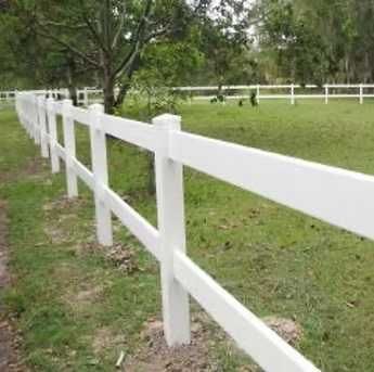White wooden fence running through a grassy park with trees in the background