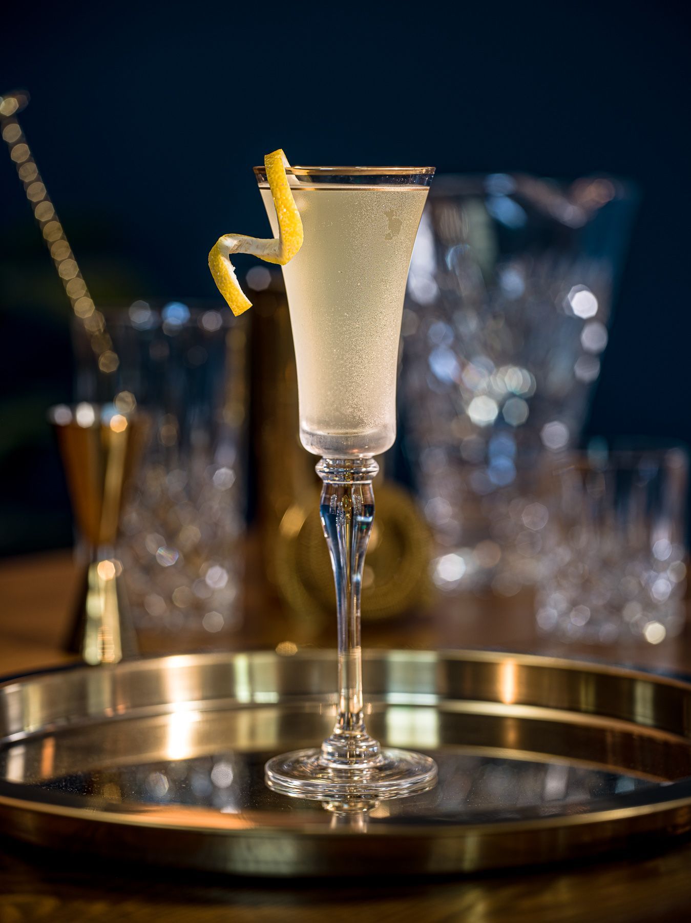 A glass of champagne with a lemon peel on top is on a tray.