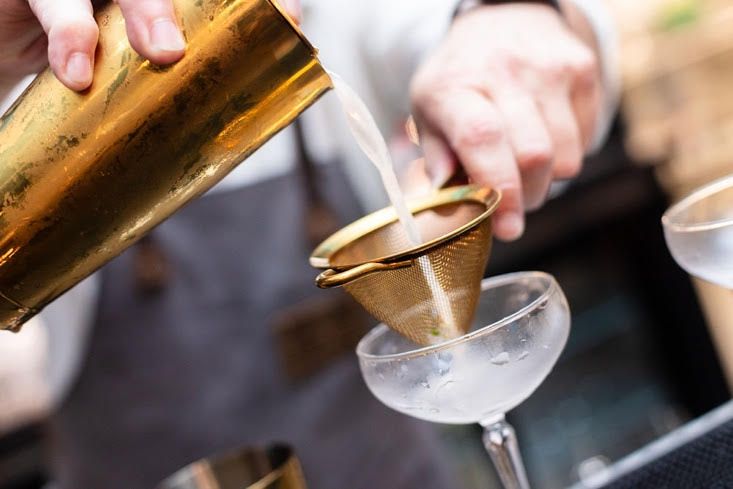 A bartender is pouring a drink into a martini glass.