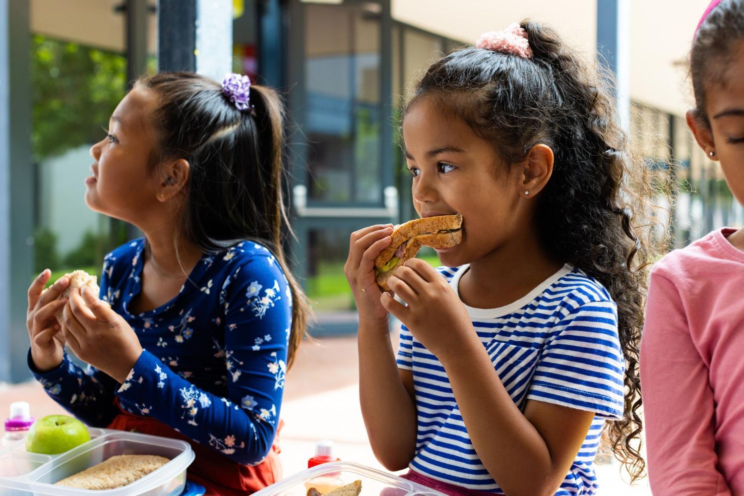 Three young girls are sitting at a table eating lunch.