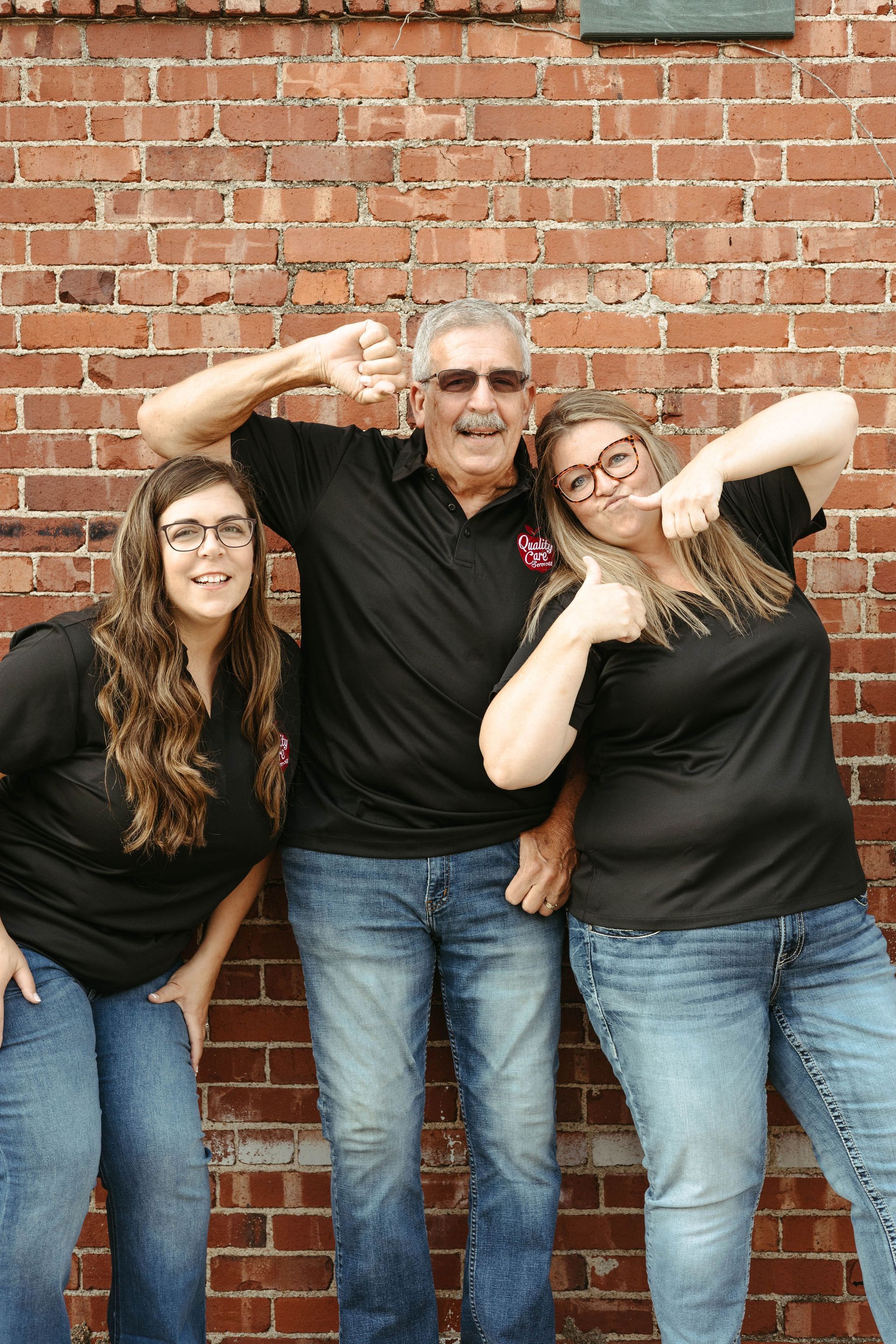 A man and two women are posing for a picture in front of a brick wall.