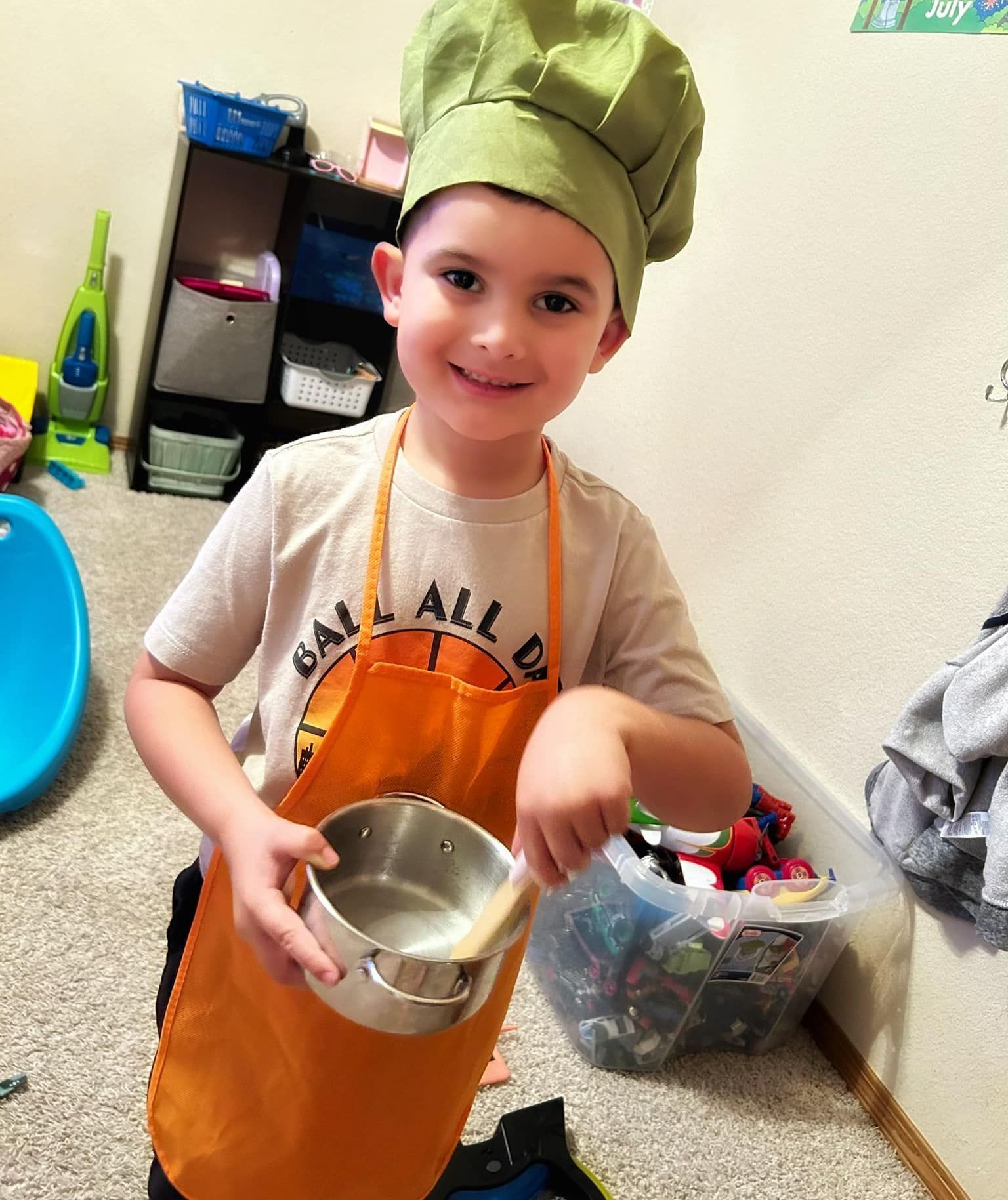 A young boy wearing a chef 's hat and apron is holding a pot.