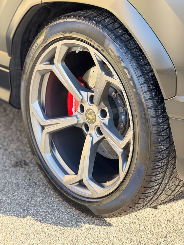 Close-up of a silver car wheel with a red brake caliper on a sunlit road.