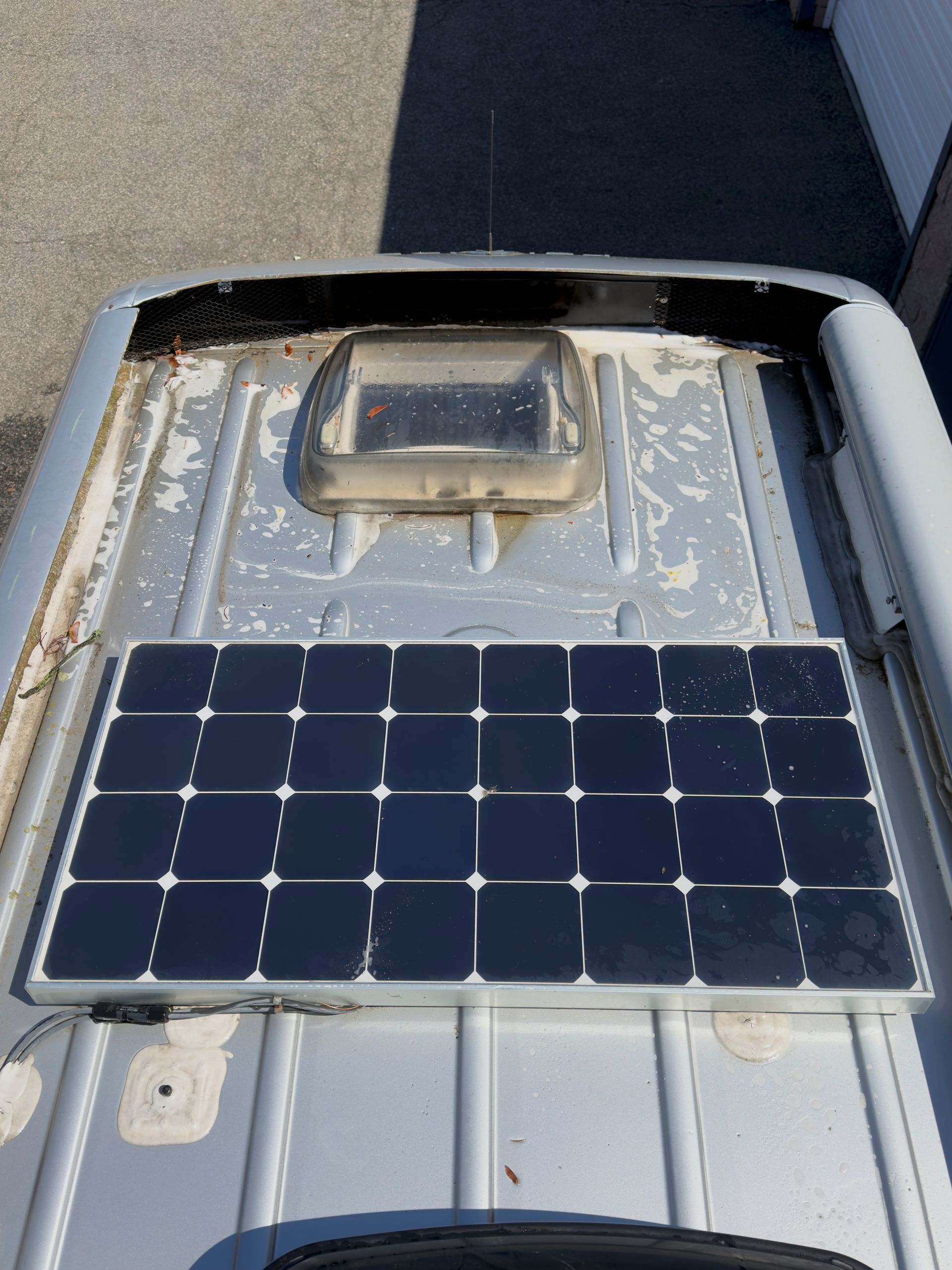 Solar panel mounted on a gray metal surface with a small vent and dark frame around it