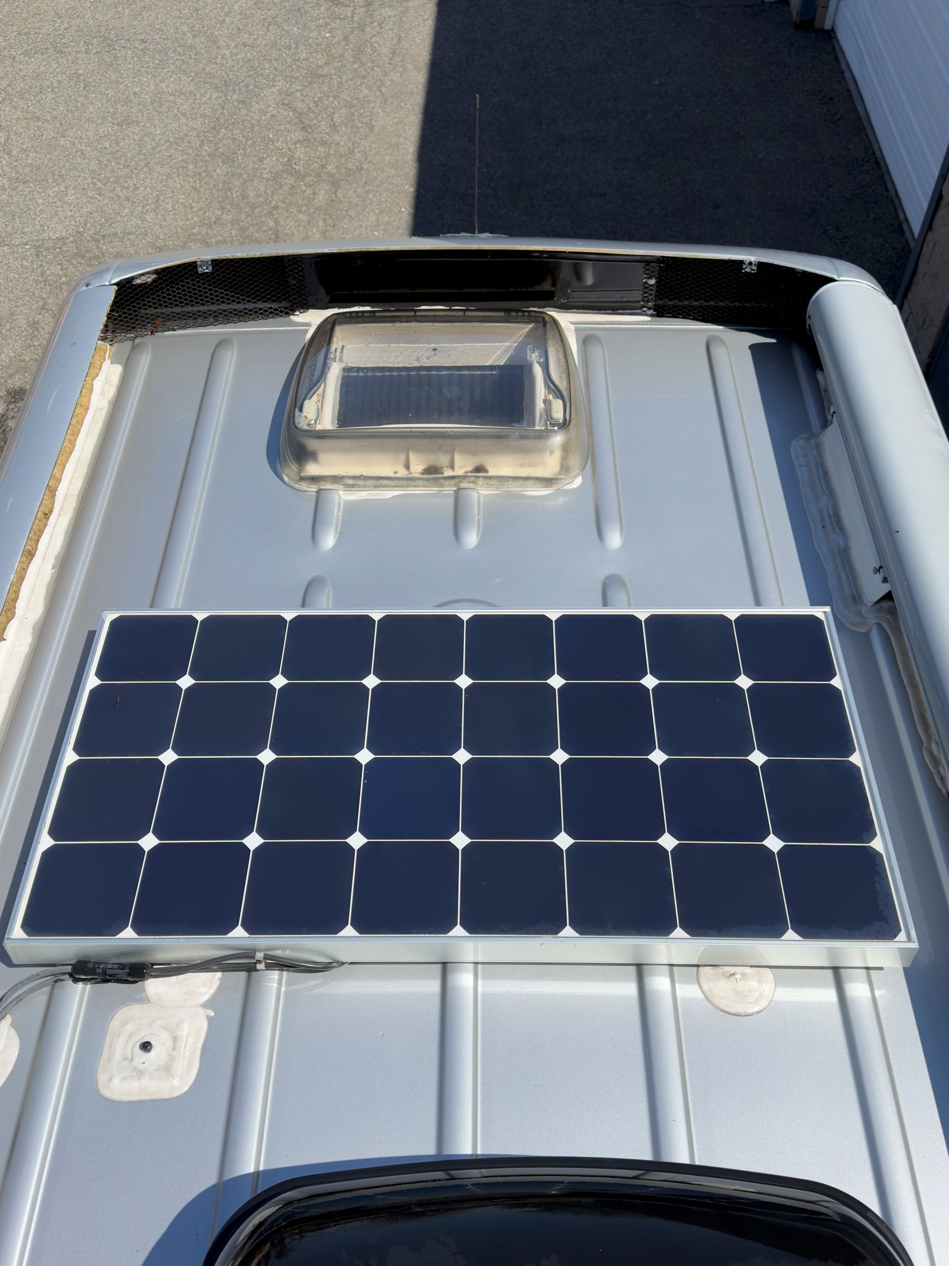 Solar panel mounted on a ribbed gray metal roof with a skylight.
