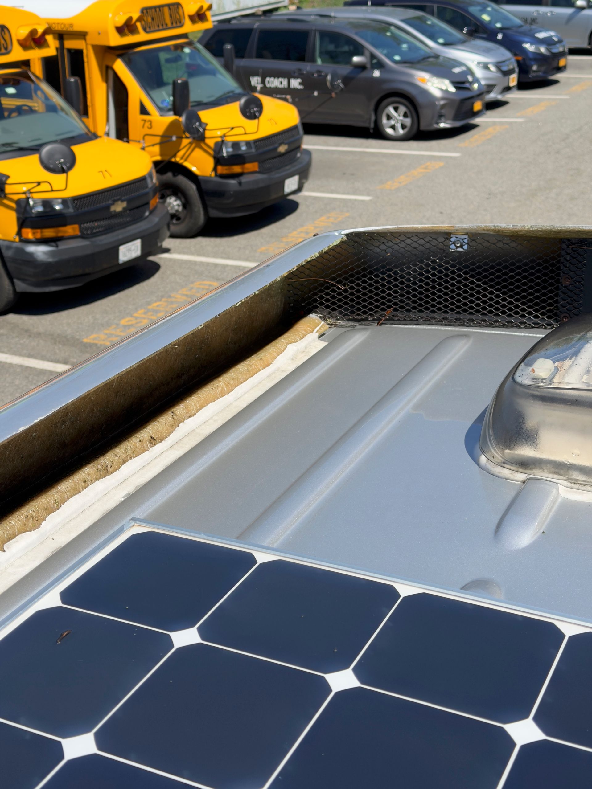 Solar panels on a vehicle bed, with parked yellow vans in the background.