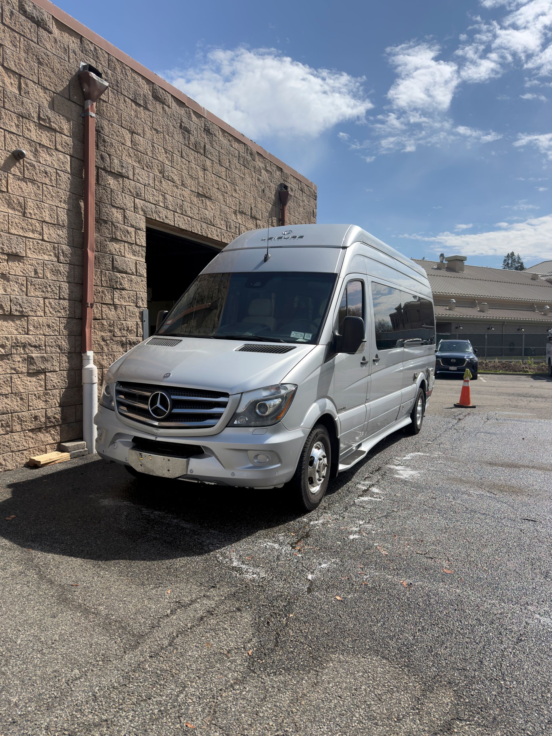 Silver Mercedes Sprinter van parked beside a stone building on a gravel lot under a blue sky