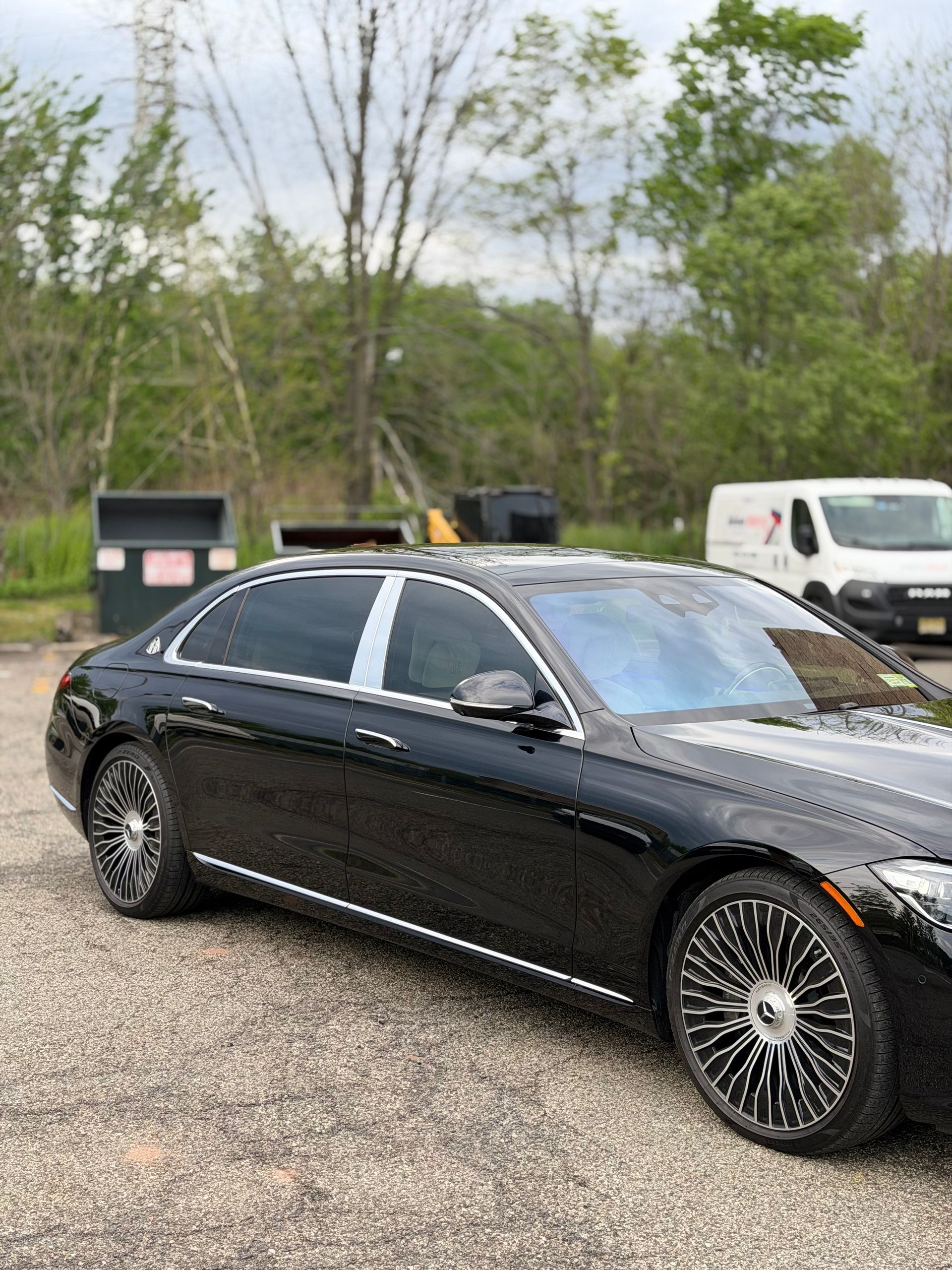 Black sedan parked on gravel near trees, with a white van in the background.