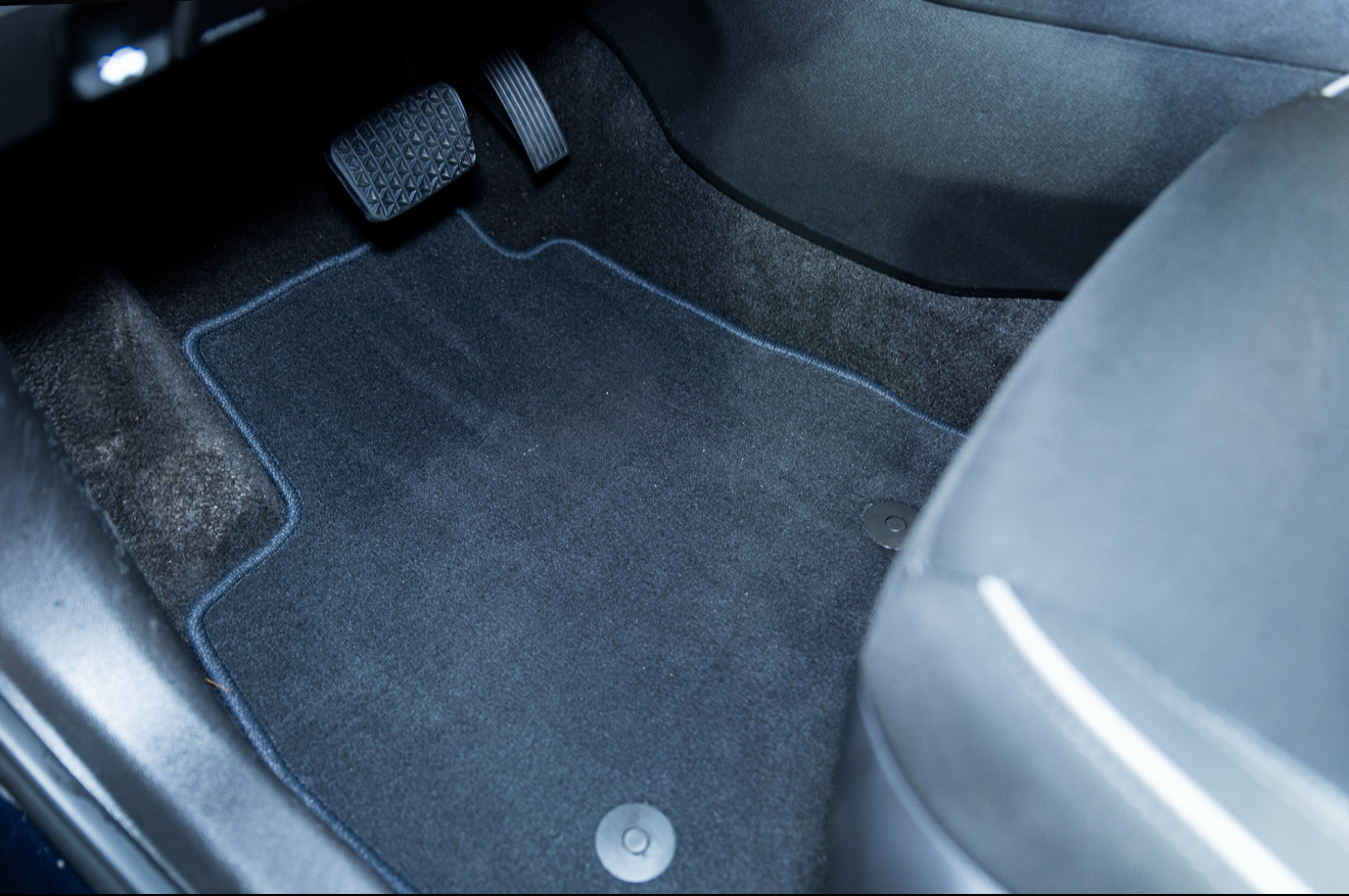 Car’s front footwell with black floor mat and pedals visible