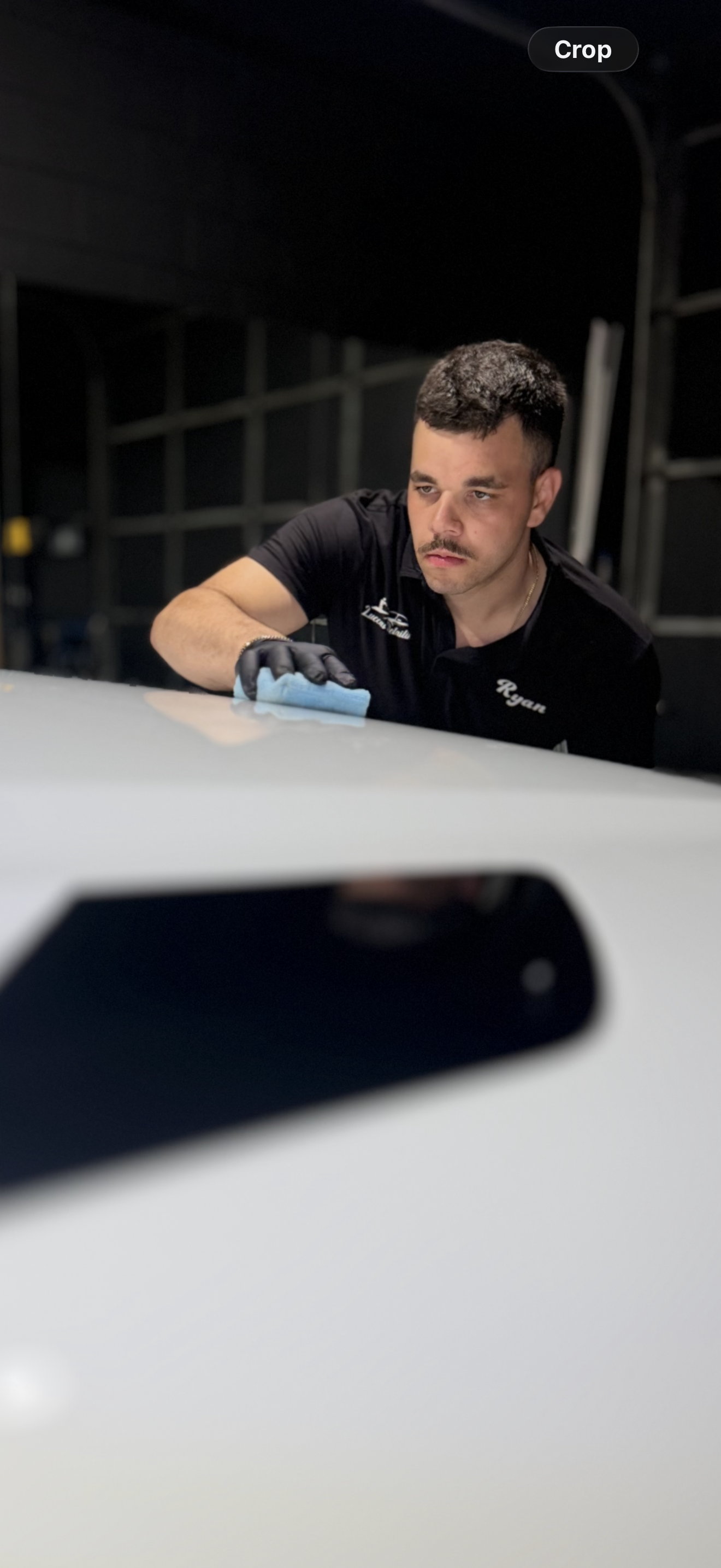 Gloved hand buffing a yellow car’s glossy surface with a sponge in a garage
