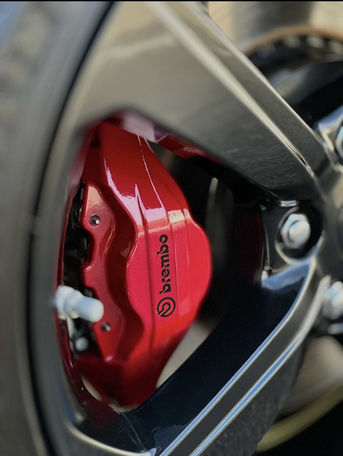 Close-up of a car wheel with silver spokes, red brake caliper, and black tire