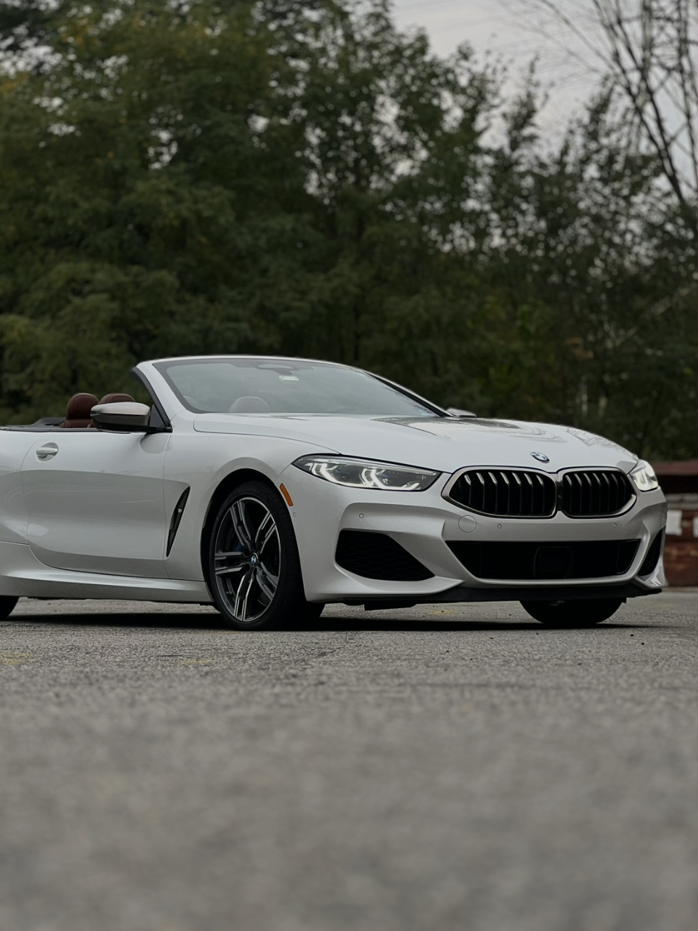White BMW convertible parked on pavement with trees in the background