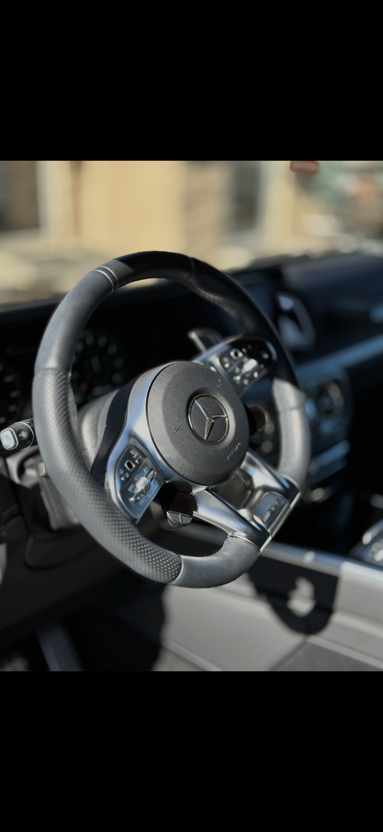 Close-up of a black steering wheel in a car interior with sunlight and blurred background