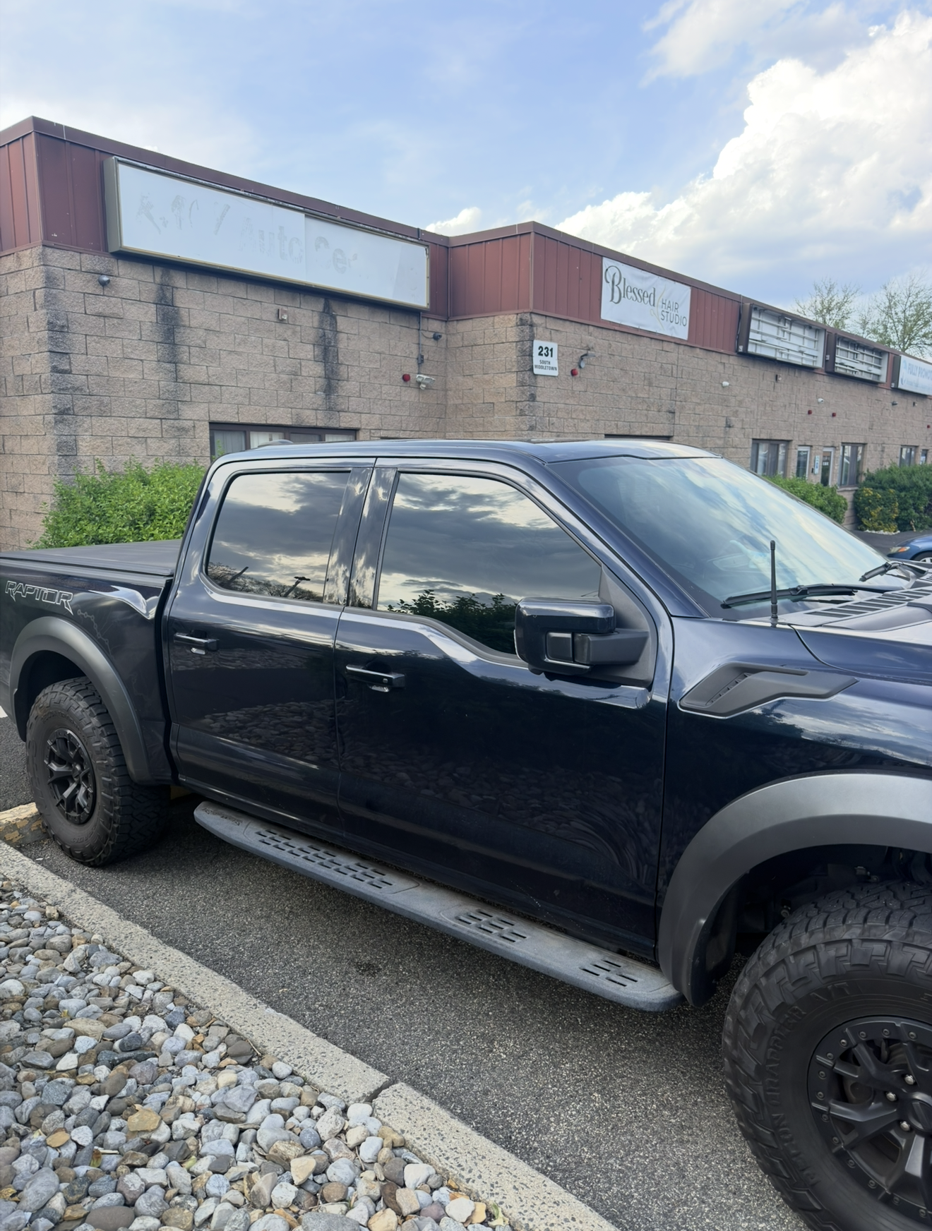 Black pickup truck parked on gravel in front of a modern building under a partly cloudy sky
