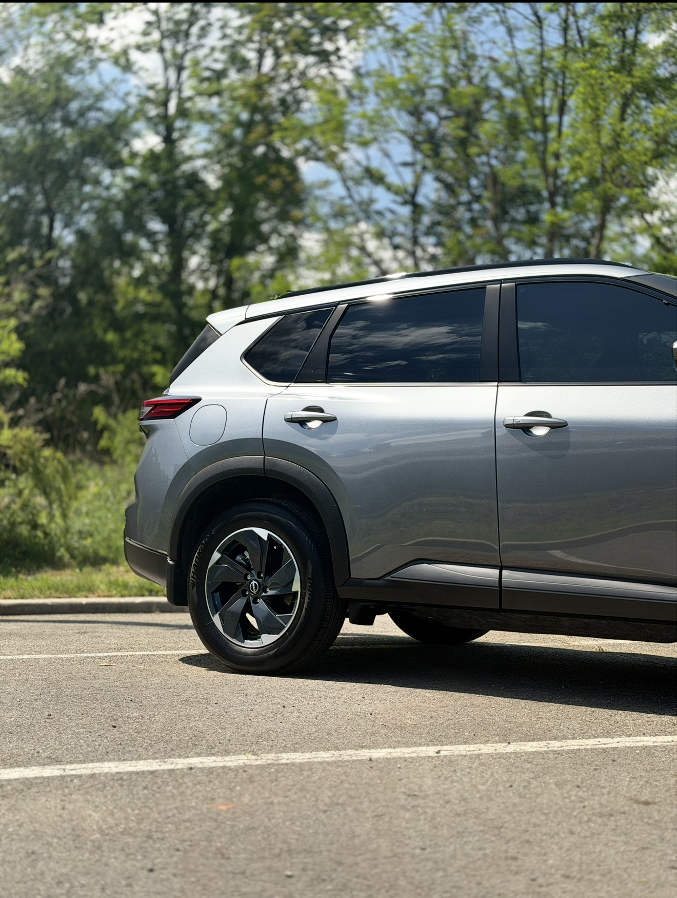 Silver SUV parked by a tree-lined road in bright sunlight