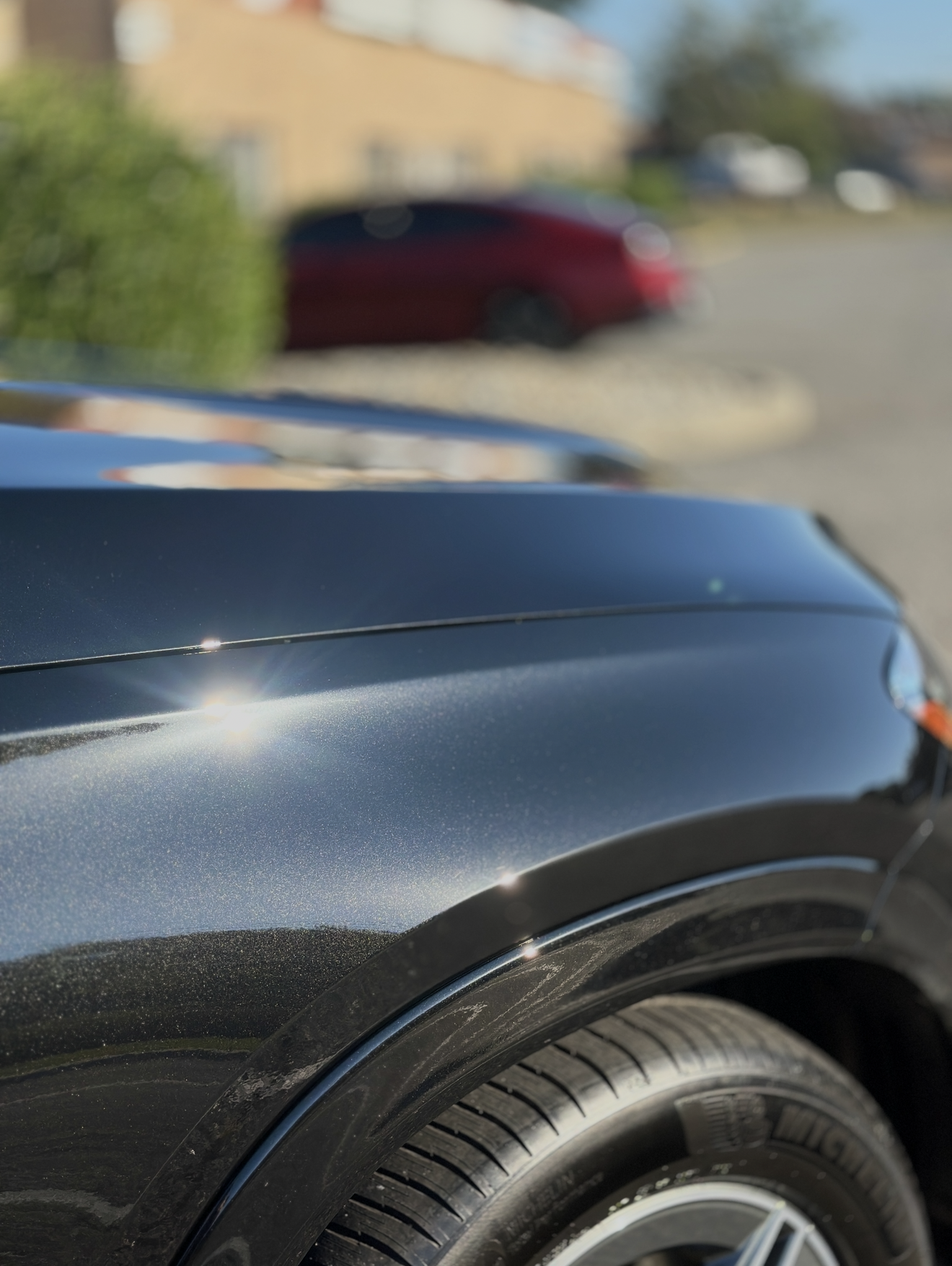 Person polishing a black car with a buffer near the headlight.