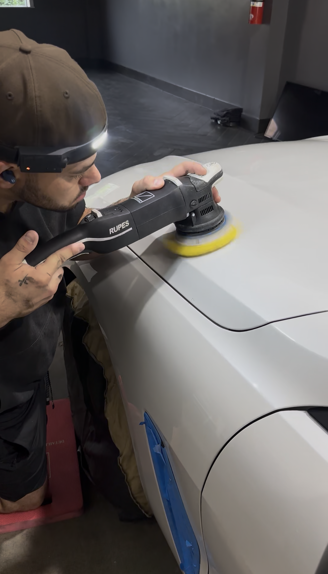 Person using a buffer to polish a white car hood in a garage