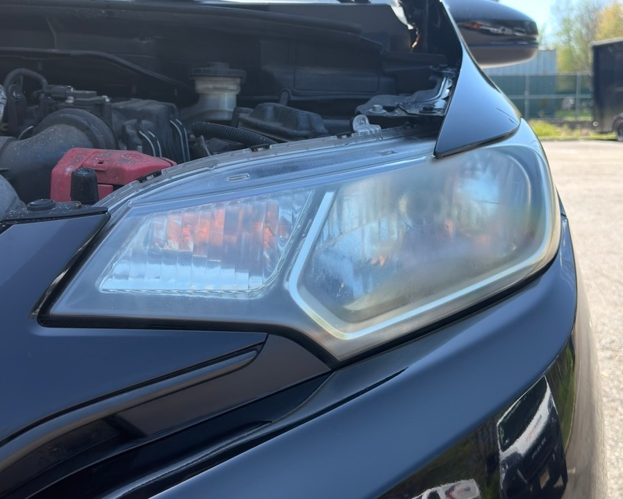 Close-up of a car’s front headlight and open hood in daylight